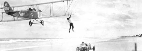 Mabel Cody transfers from car to airplane wing at Daytona Beach in 1921